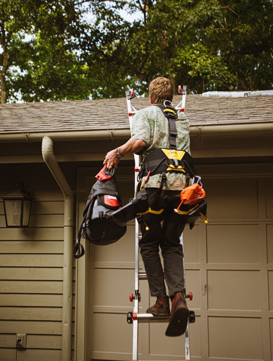 Technician on a ladder checking a roofline and gutter on a suburban home