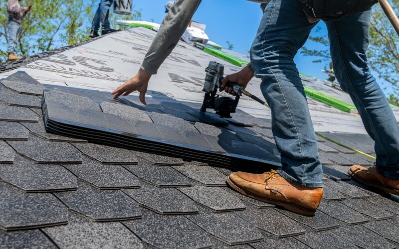 Roofer fixing asphalt shingles with a nail gun